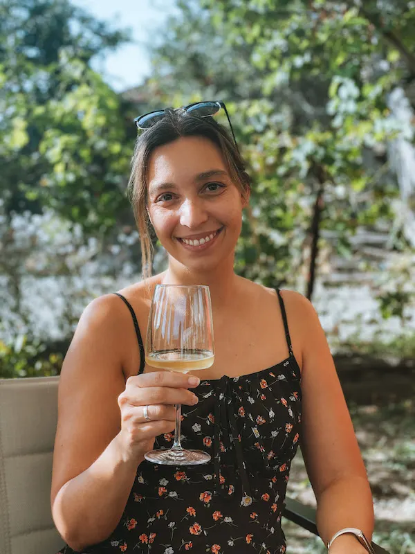 A woman smiling to camera, holding a glass of white wine