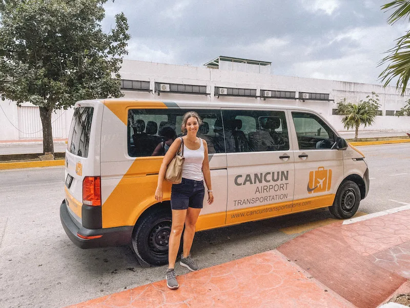 Woman smiling and standing in front of a white and yellow van with the Cancun Airport Transportation logo.