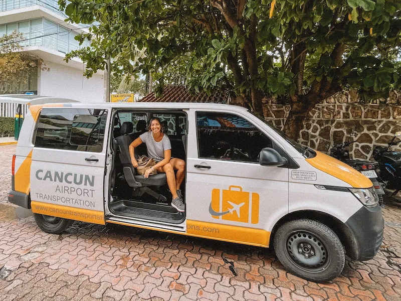 Smiling woman sitting inside a van with the Cancun Airport Transportation logo.