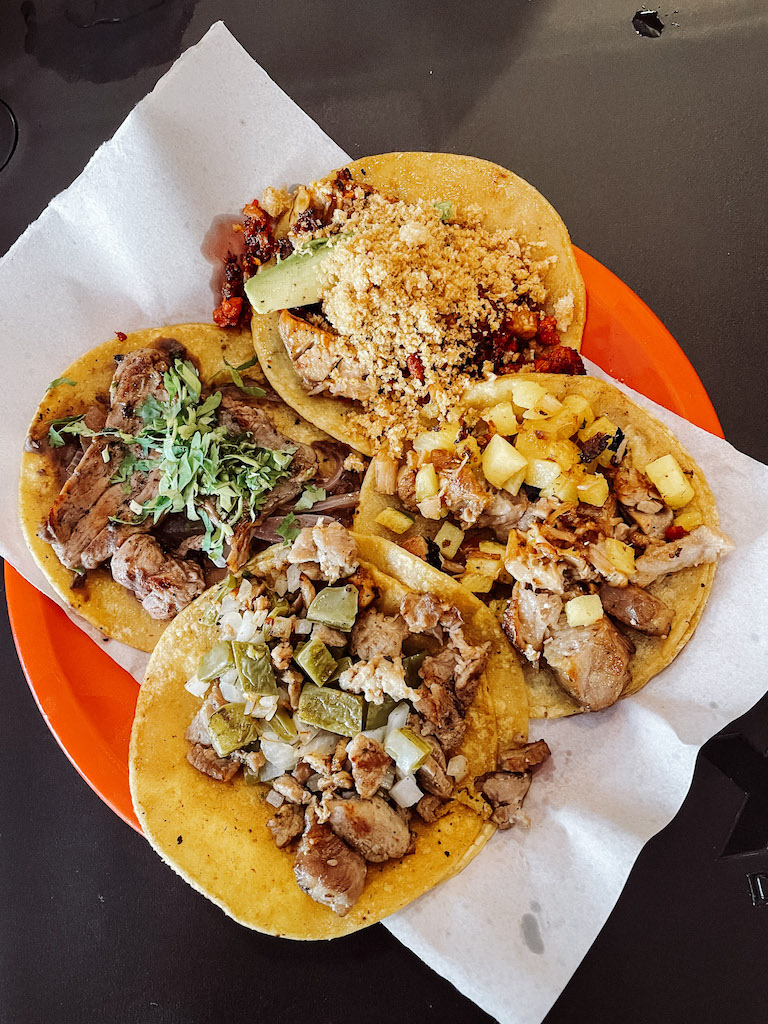 Red plate with four corn tacos with different condiments on them.