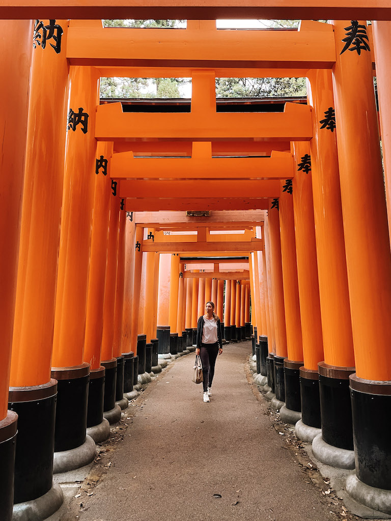 Woman standing under the orange squared arches of Fushimi Inari shrine in Kyoto.
