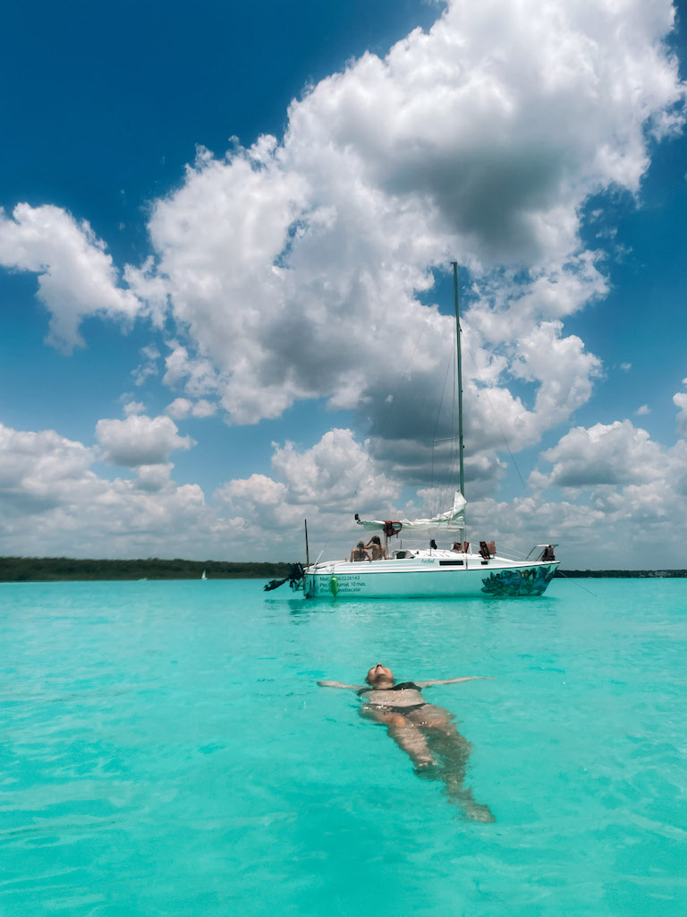 Woman in a brown bikini floating on the sea with a catamaran in the background.