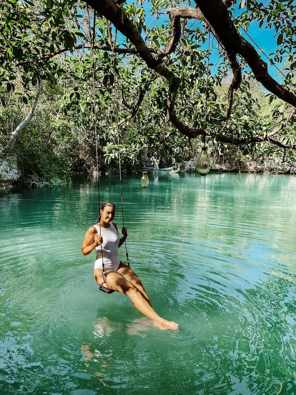 A woman wearing a white swimsuit sitting on a swing over a cenote