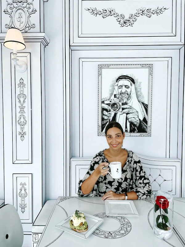 Woman smiling at the camera and holding a cap in a 2D cafe in Dubai.