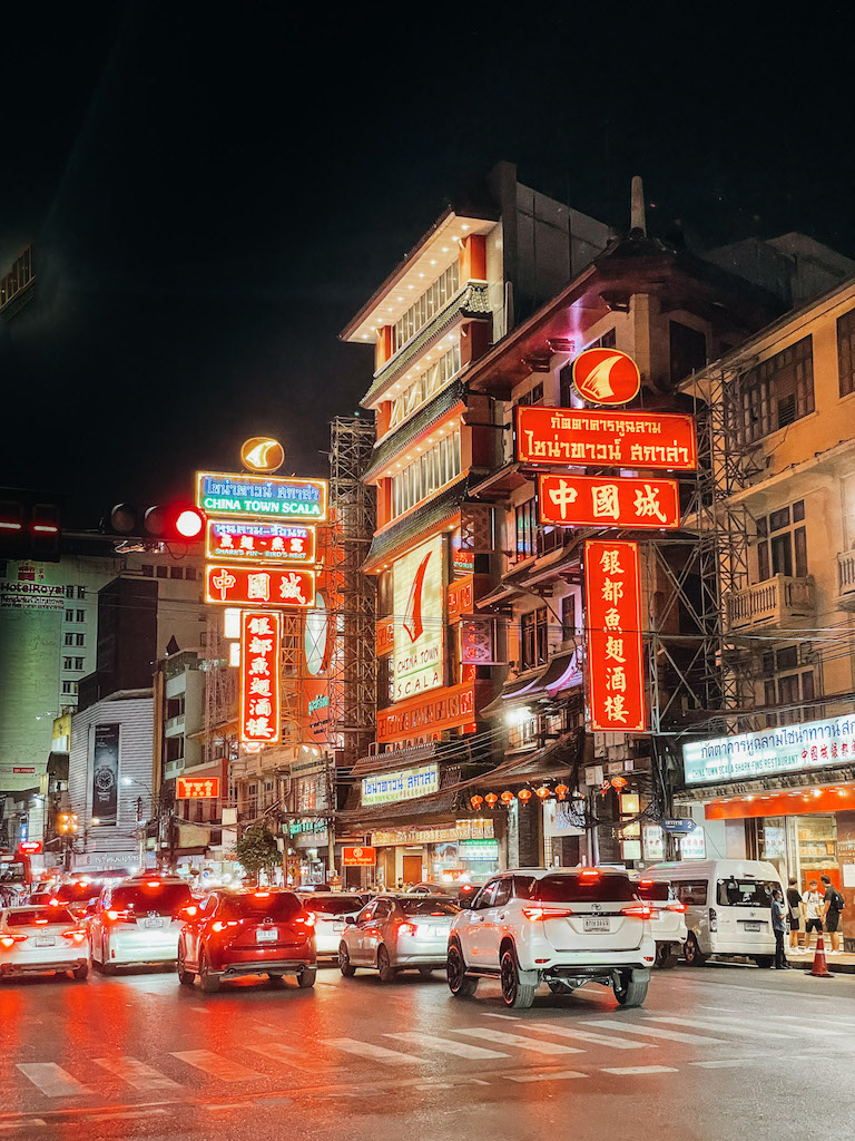 A street with red neon signs and cars at night, inserted in a post about the best Bangkok tours