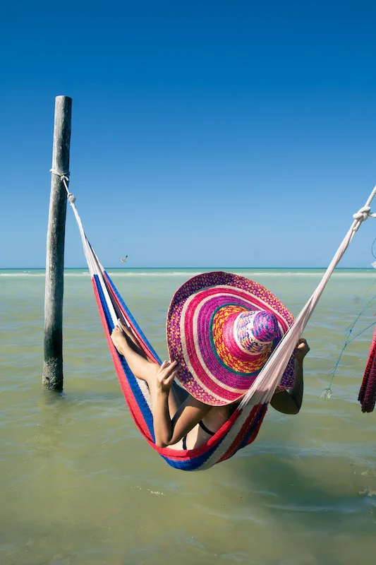 Woman with a coorful Mexican hat laying on a hammock on the water