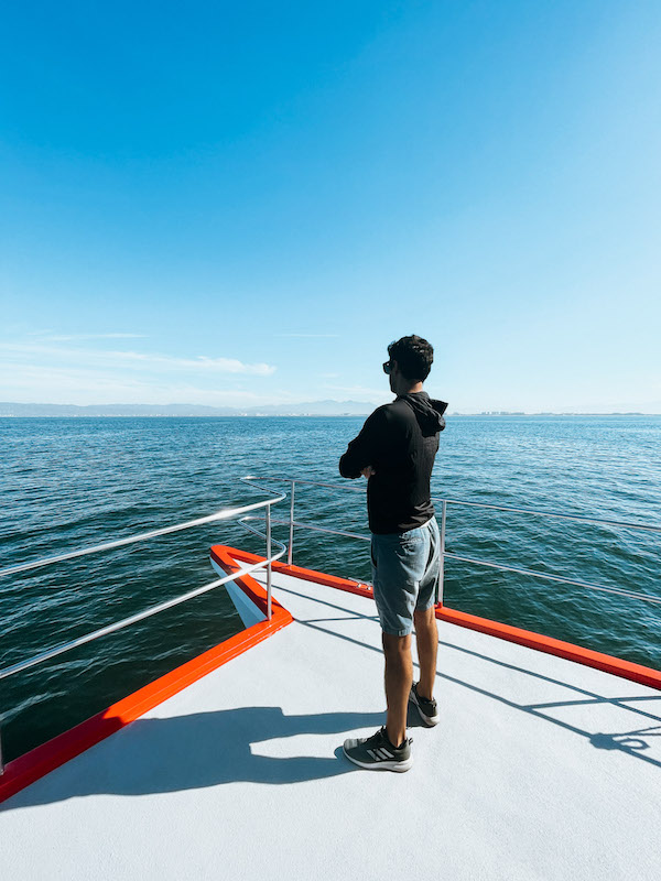 A man standing on a boat's deck, looking out at the ocean