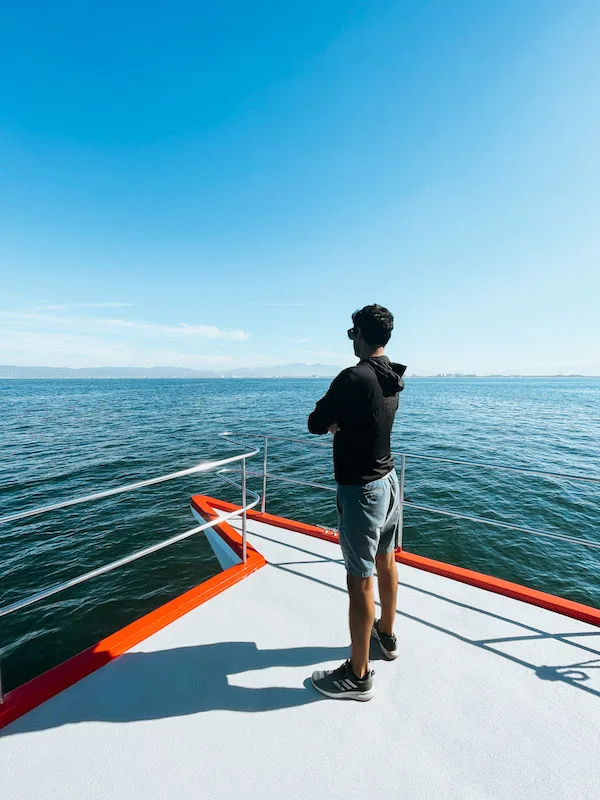 A man standing on a boat's deck, looking out at the ocean