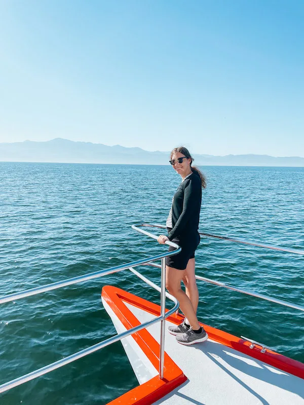 Girl standing at the end of a catamaran, smiling to the camera.