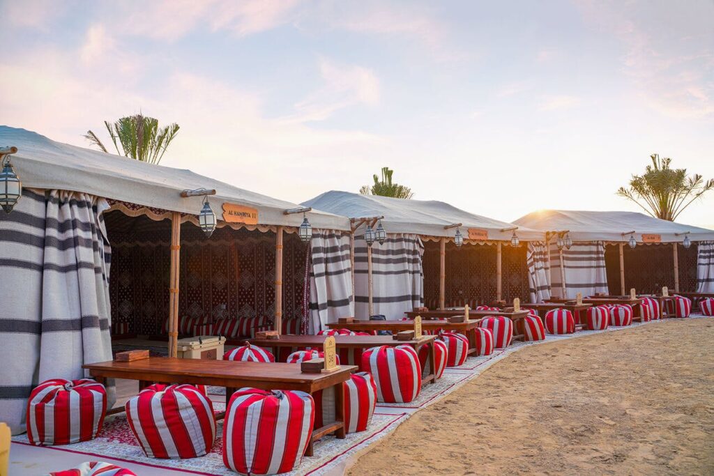 Image of desert tents, and tables with striped pouf seats around them, inserted in a post about Dubai Desert Resorts & Hotels