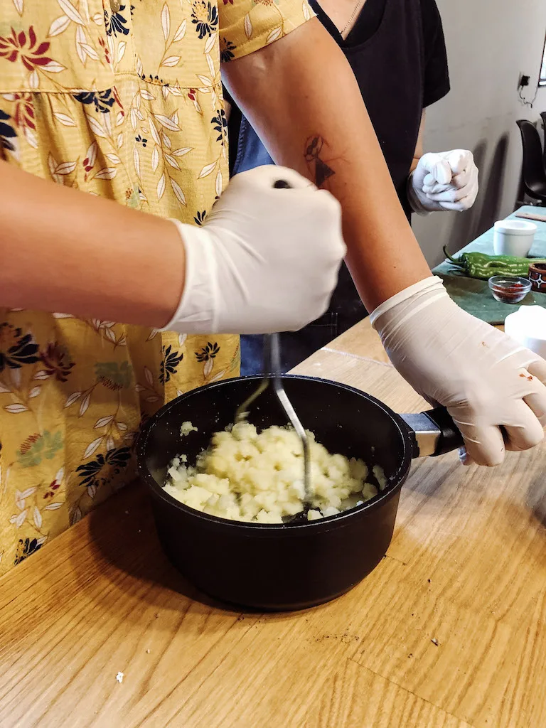 Hands with latex gloves mashing potatoes in a black pot