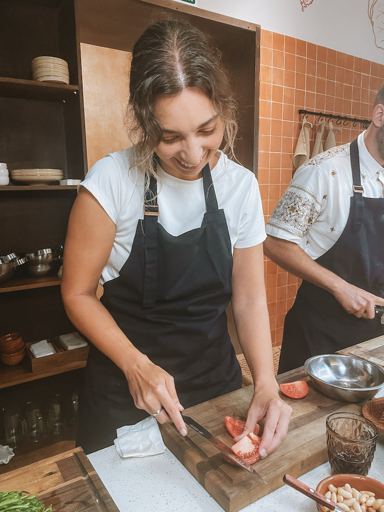 A woman wearing a black apron chopping a tomato on a wood cutting board 