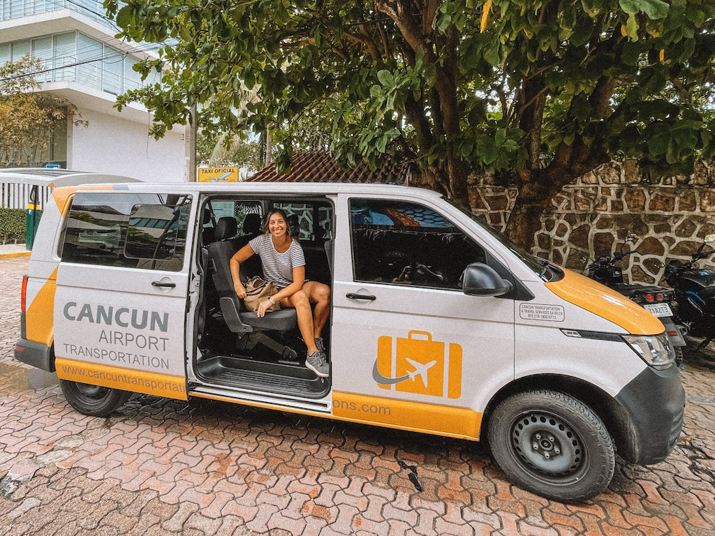 Woman smiling sitting inside a white and yellow van branded Cancun Airport Transportation.