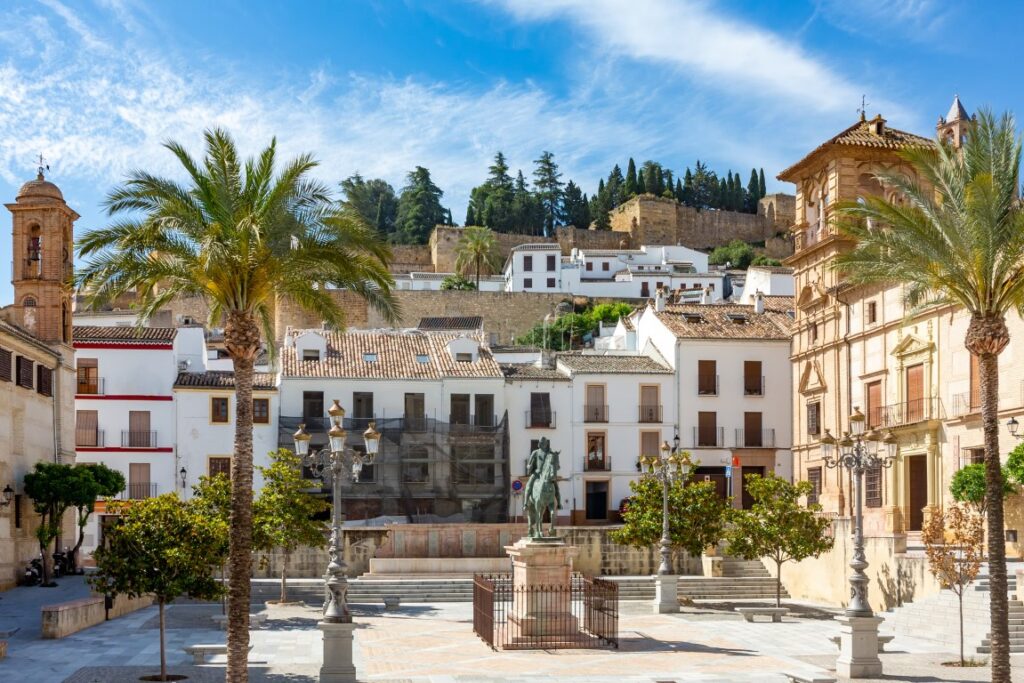 The Square of Don Fernando in Antequera, with white buildings around it, a statue in the center, and palm trees