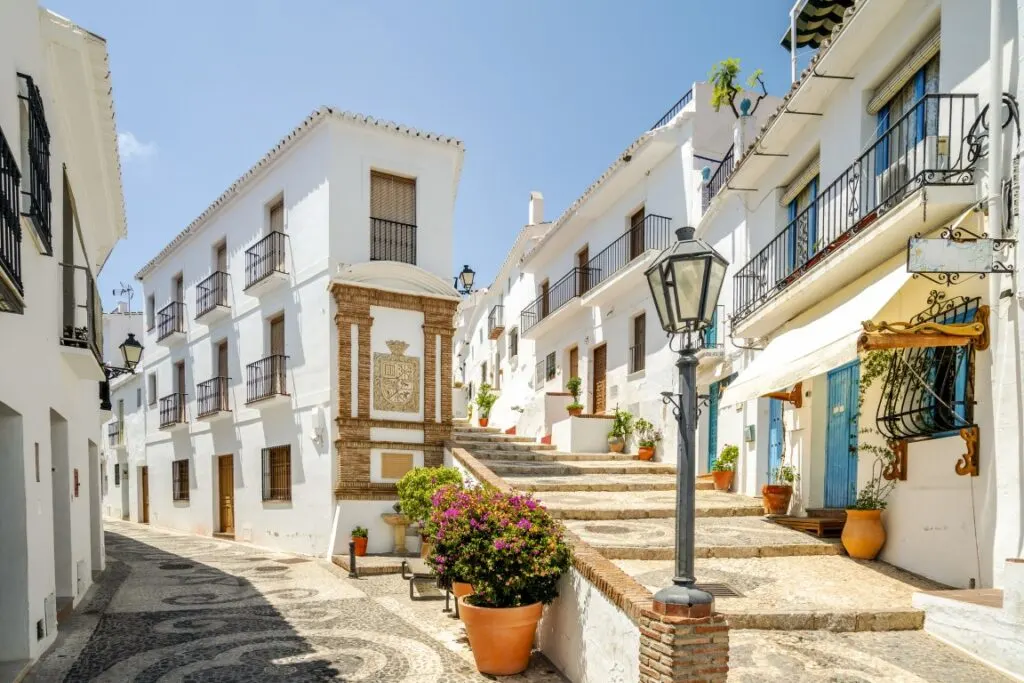 A cobblestone street in the town of Frigiliana, with white-washed houses, a street lamp, and flower pots