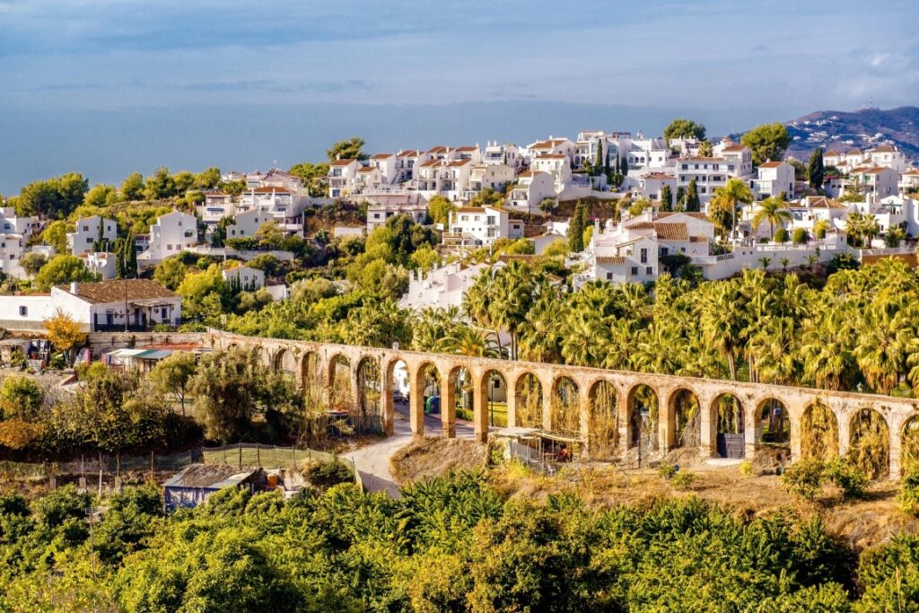 The town of Nerja surrounded by green palm trees and with an ancient aqueduct at the forefront