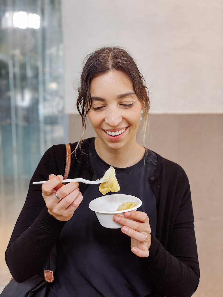 A woman eating fresh pasta out of a paper plate