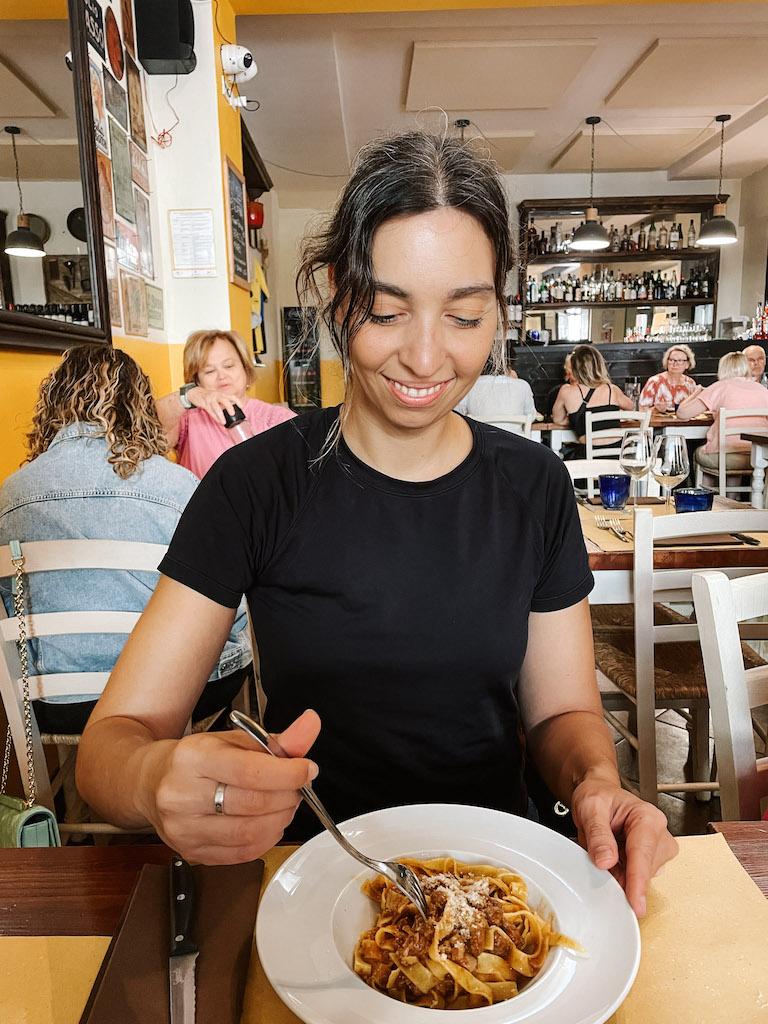 A woman eating a plate of Tagliatelle with ragu sauce