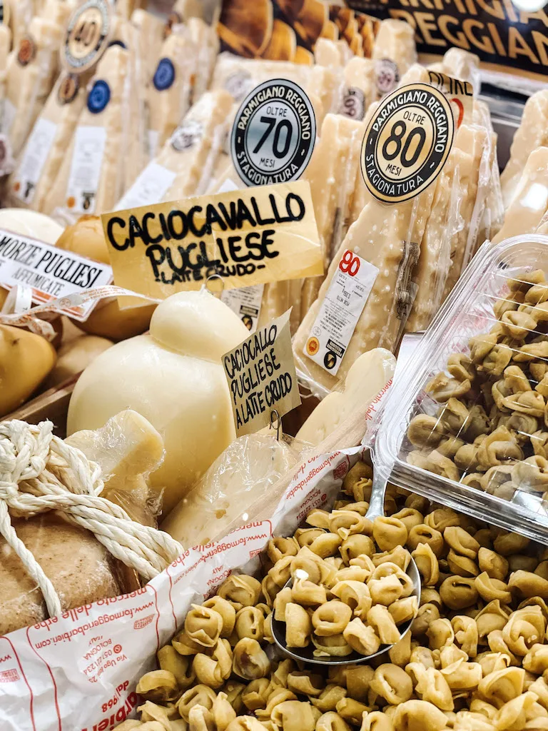 fresh  pasta on display at a food market, with cheeses right next to it 