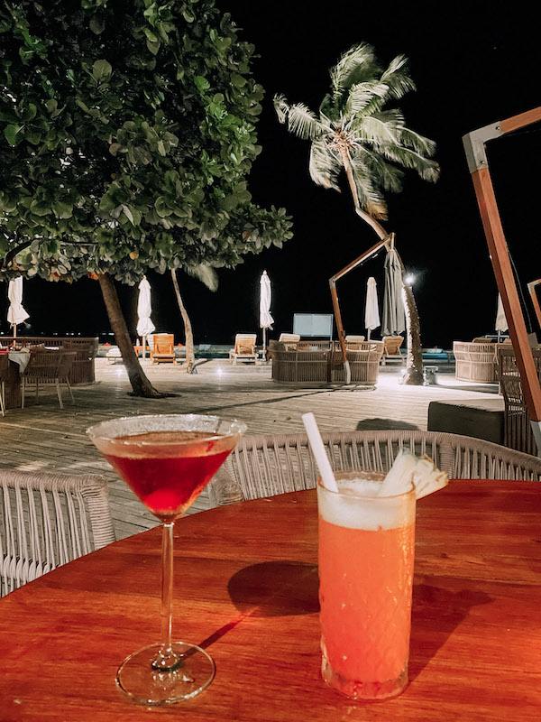 Two cocktails set on a table, and the beach behind it