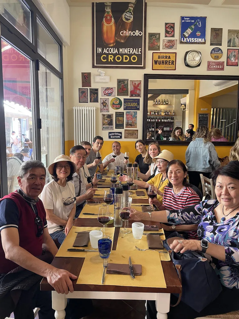 A long table with people sitting around it, holding wine glasses and smiling at the camera