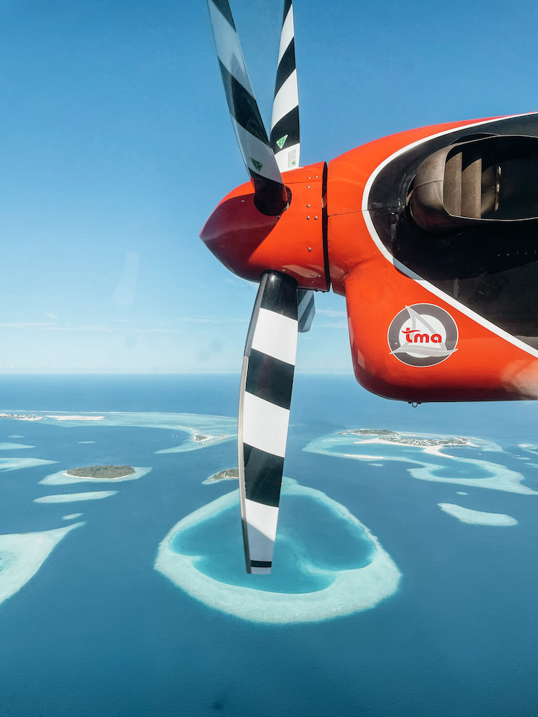 Close up image of a sea plane's propeller and atolls in the background surrounded by the sea