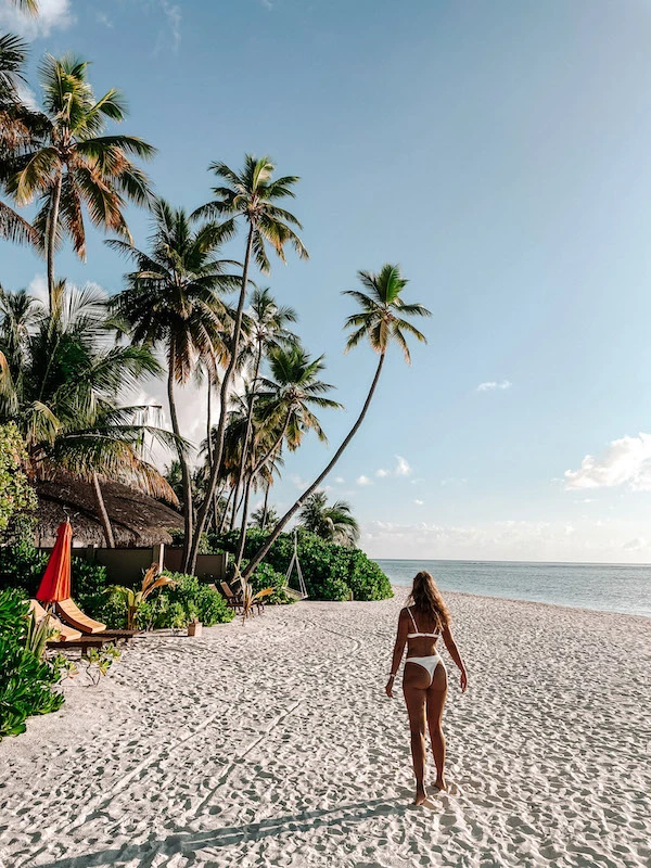 A woman in a white bikini walking along the beach 