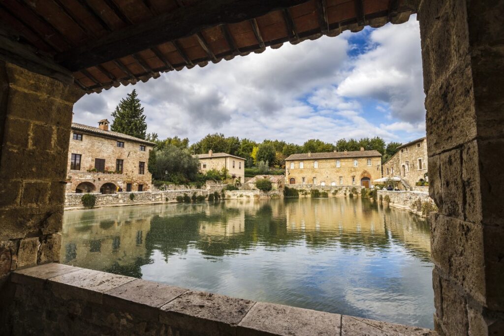 An image of  Piazza delle Sorgenti in Bagno Vignoni, with a large thermal pool in the center, and buildings around it