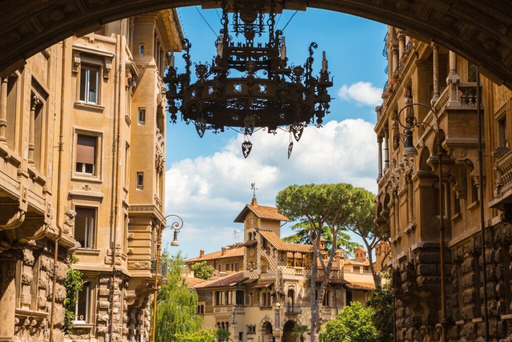 An image of Quartiere Coppede in Rome, with a chandelier hanging and an eccentric building in the background