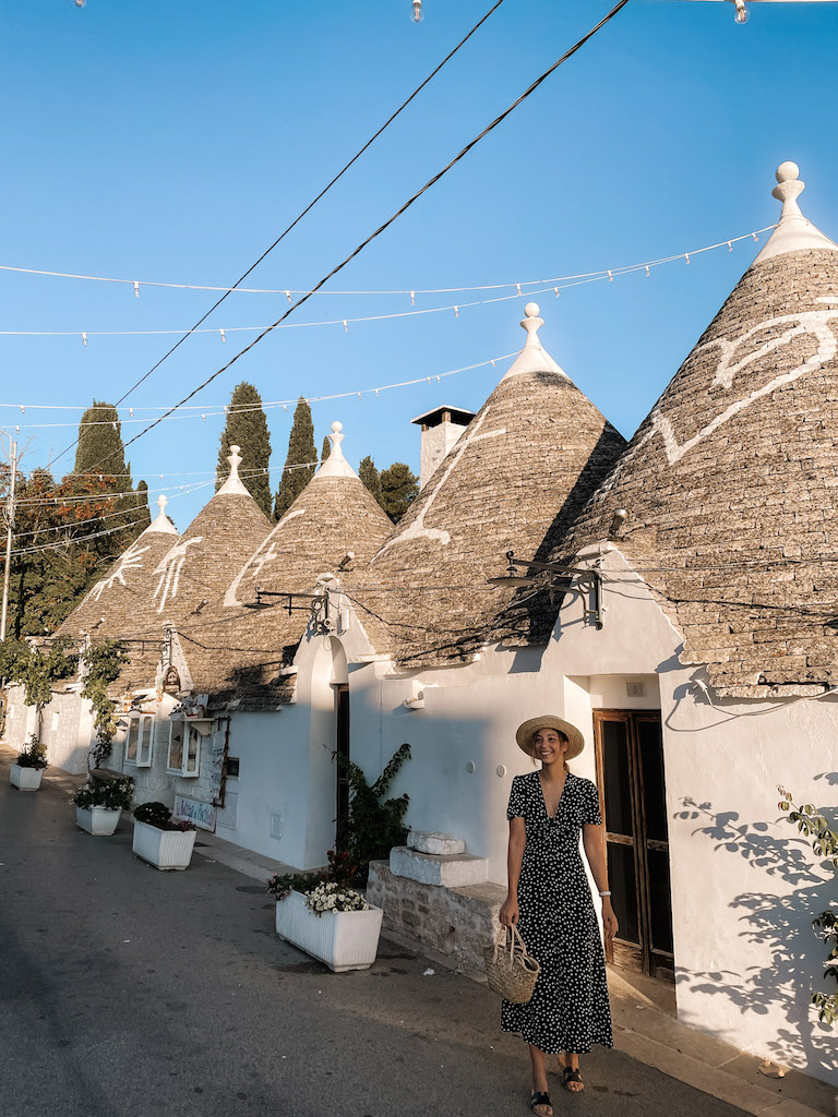 A woman in a long dress standing outside Trulli houses