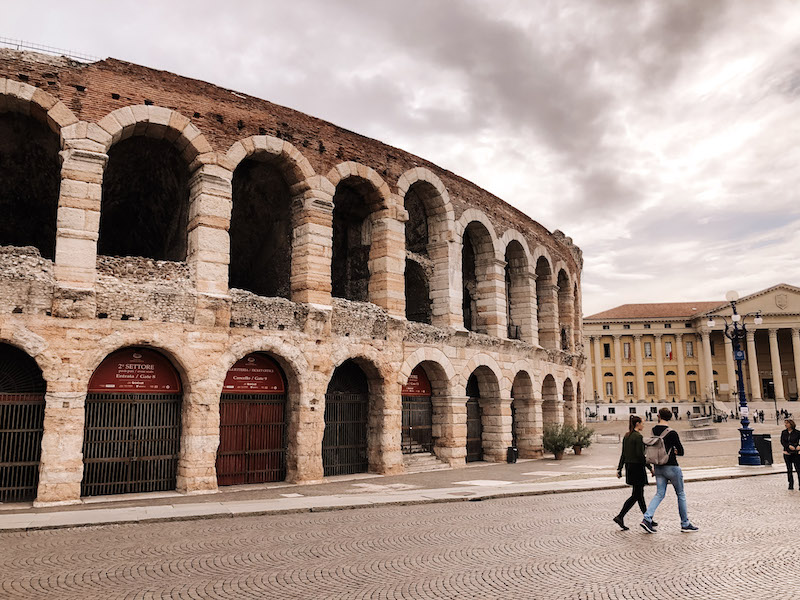 An image of the Verona Arena, and a couple walking in front of it 