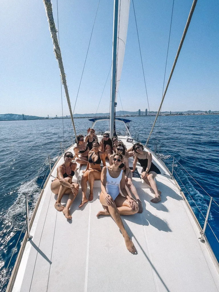 A groupf of girls looking at the camera and smiling sitting on a white sailing catamaran.