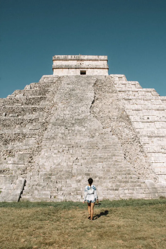 Womamn standing in front of a pyramid in Chichen Itza, from afar.