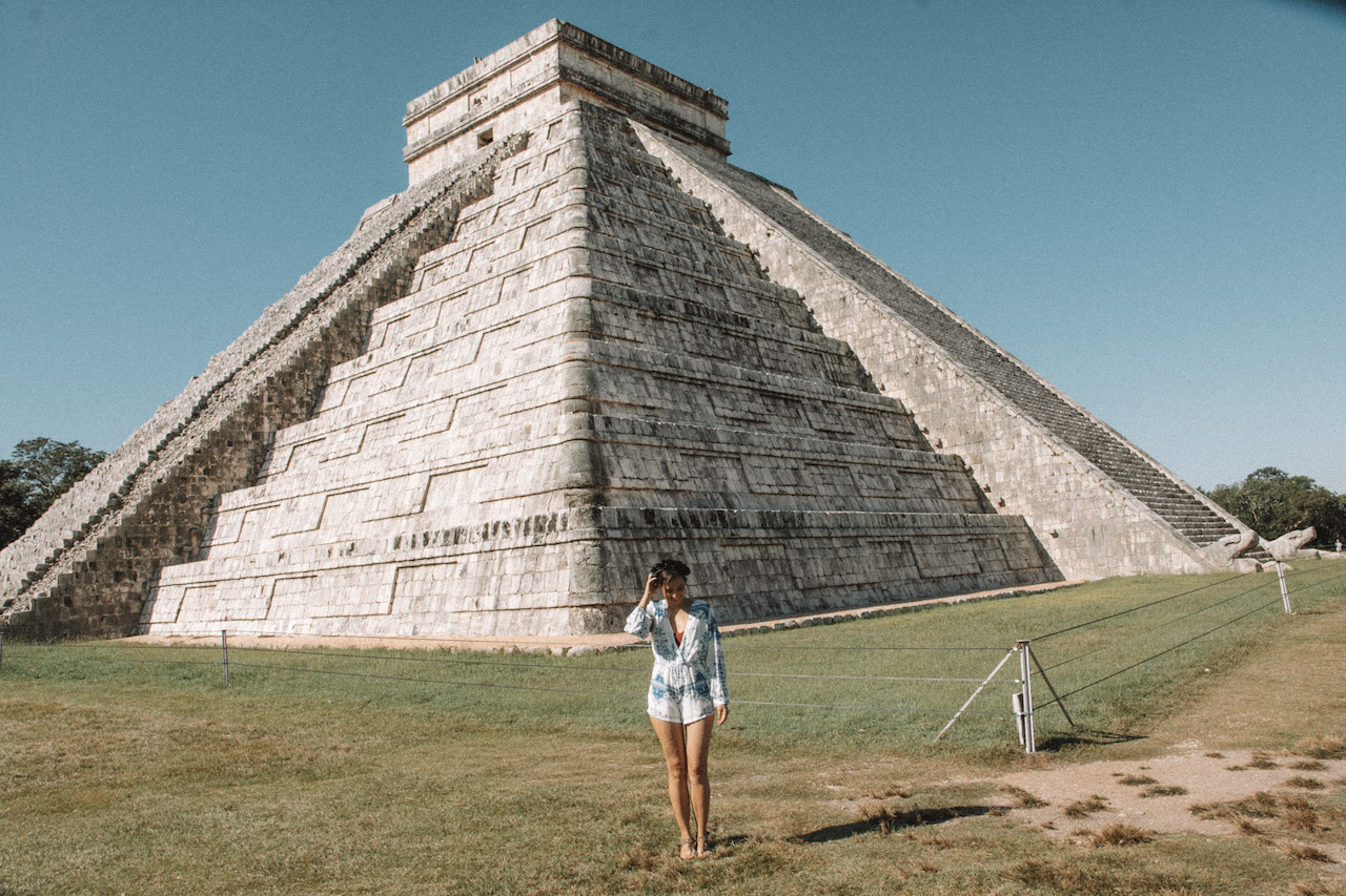 Woman with a white and blue short romper standing in front of the Kukulcan pyramid in Chichen Itza.