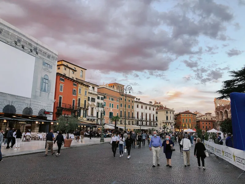 A cobblestone street in Verona, with colorful buildings on the left, and people walking along it