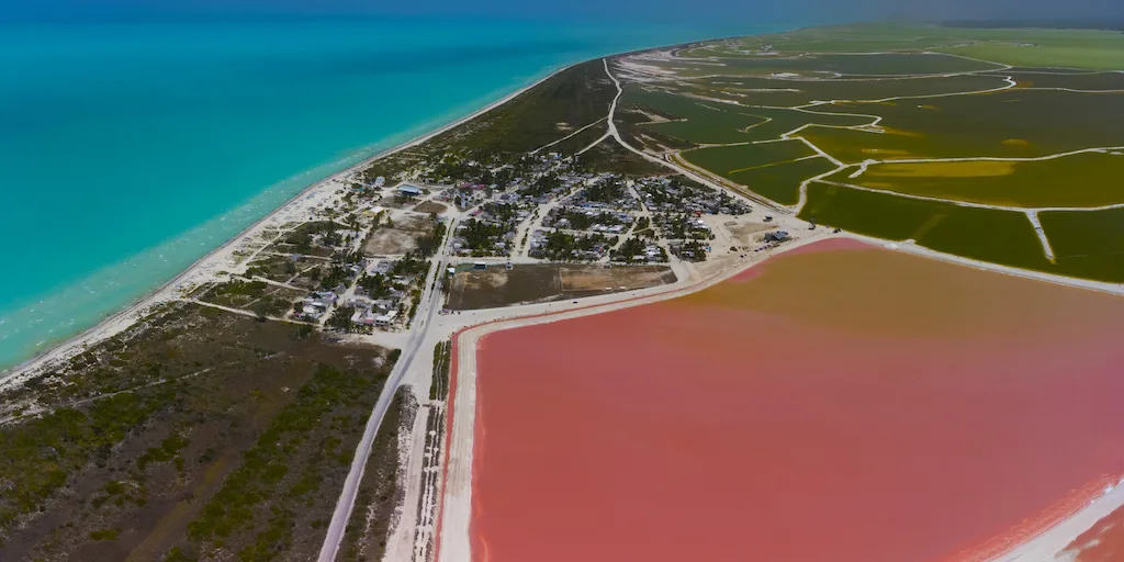 Drone photo of the pink lakes in Mexico surrounded by green fields and the ocean.