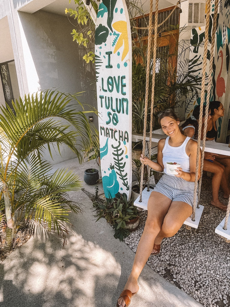 Woman smiling at the camera holding a bowl next to a sign that says 