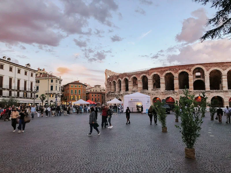 An open-air square in Verona, with the Verona Arena in the background, and people walking 