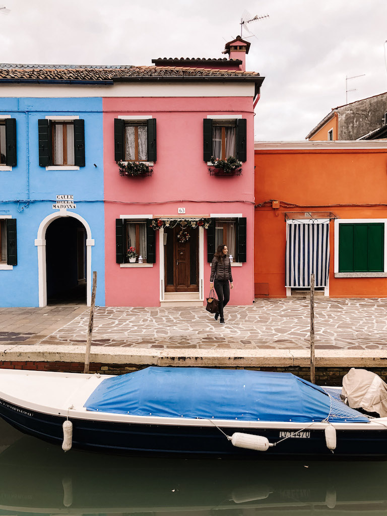 A woman standing in front of a pink house in Burano