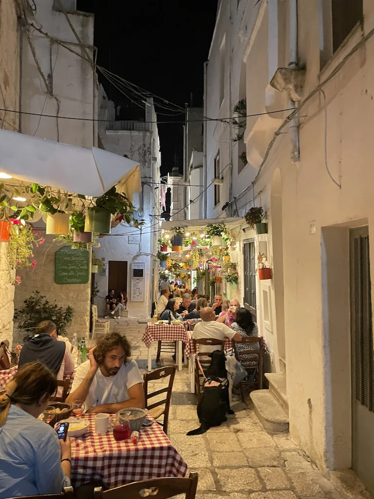 A narrow street packed with restaurant tables, and people having a meal