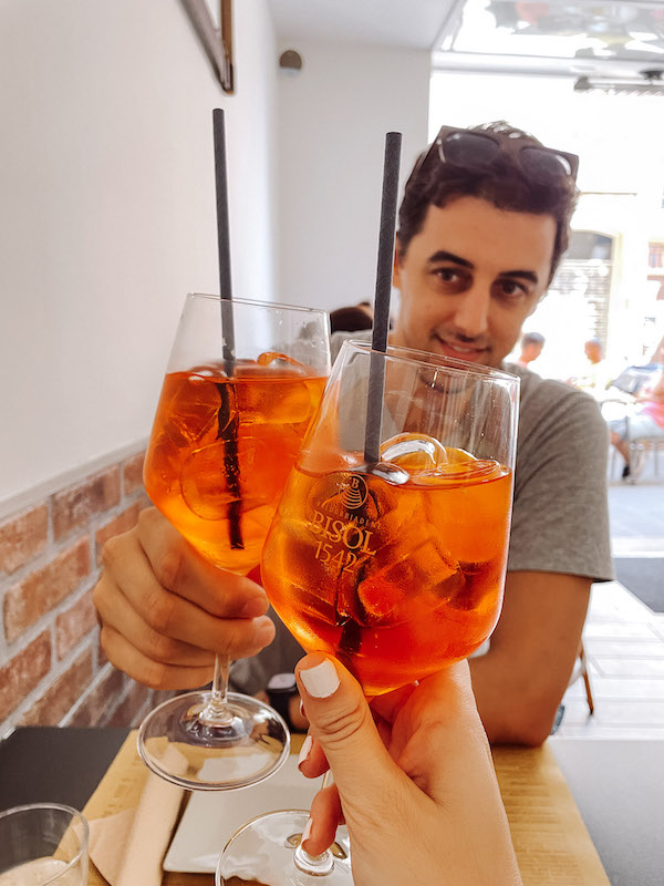 A man holding an Aperol Spritz, clinking glasses with a second glass held by a woman's hand