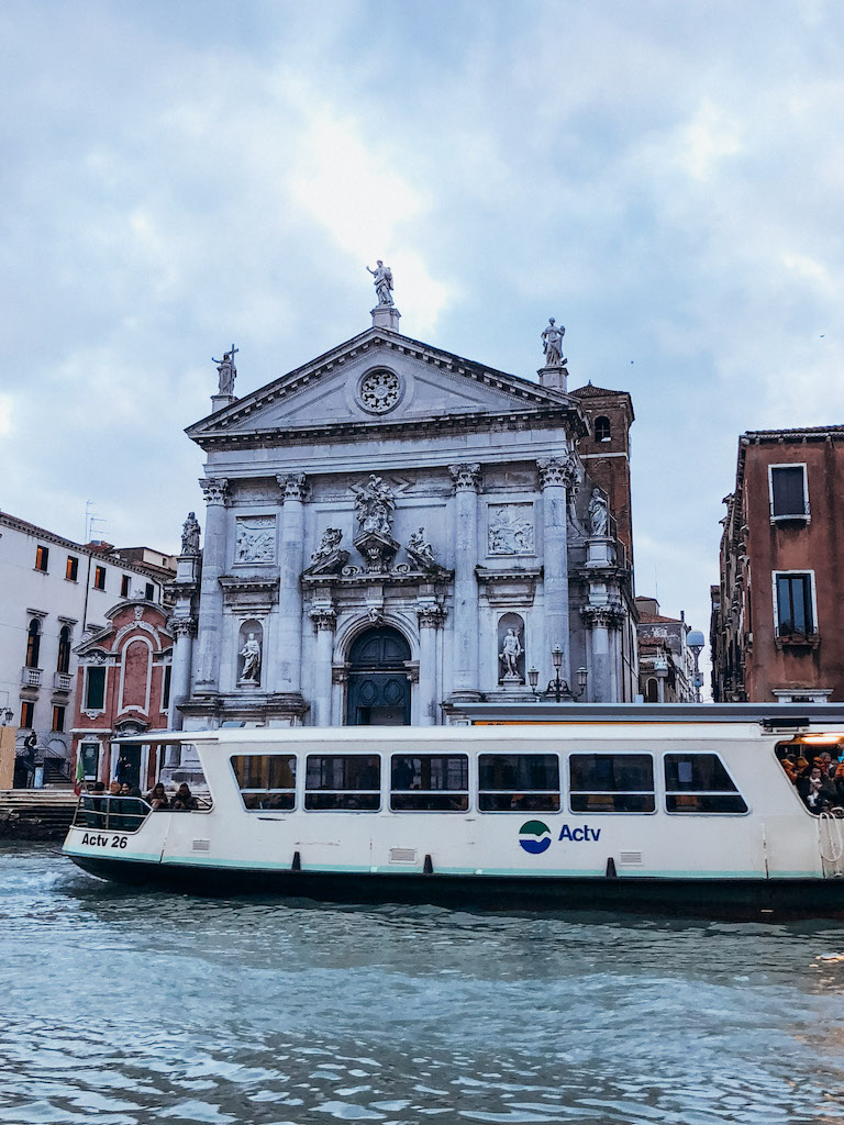 An image of a boat cruising along a canal in Venice, with a beautiful building in the background