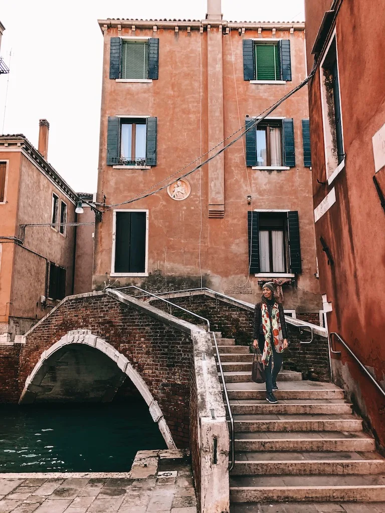 A woman standing on the steps of a small bridge spanning over a Venice canal