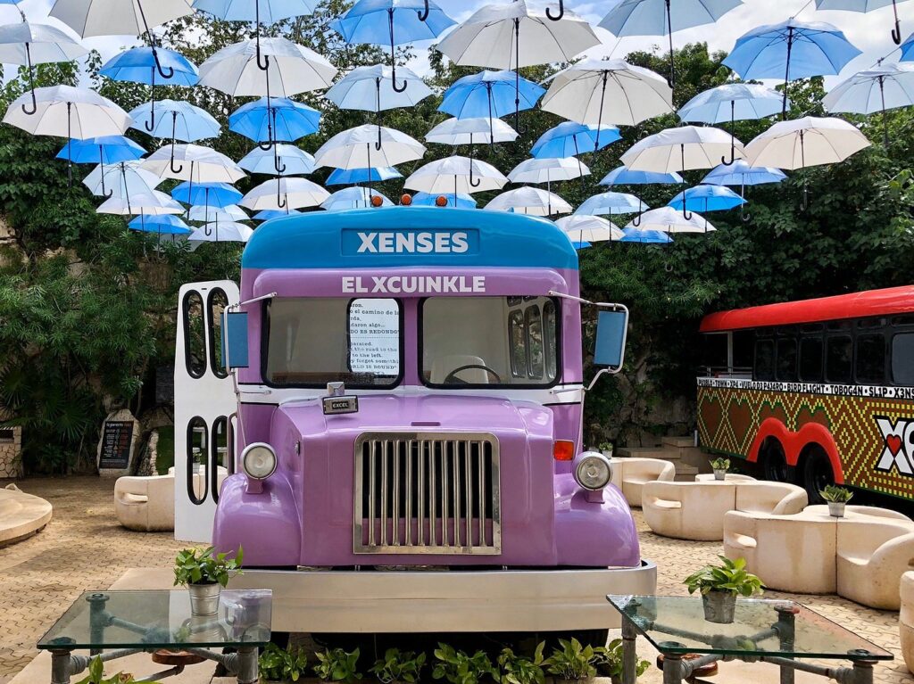 Purble and blu bus under a bunch of decorative umbrellas at Xenses park.