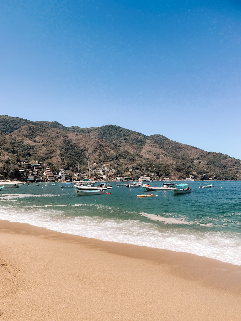 View of a bay with a bunch of boats dockes and mountains in the background.