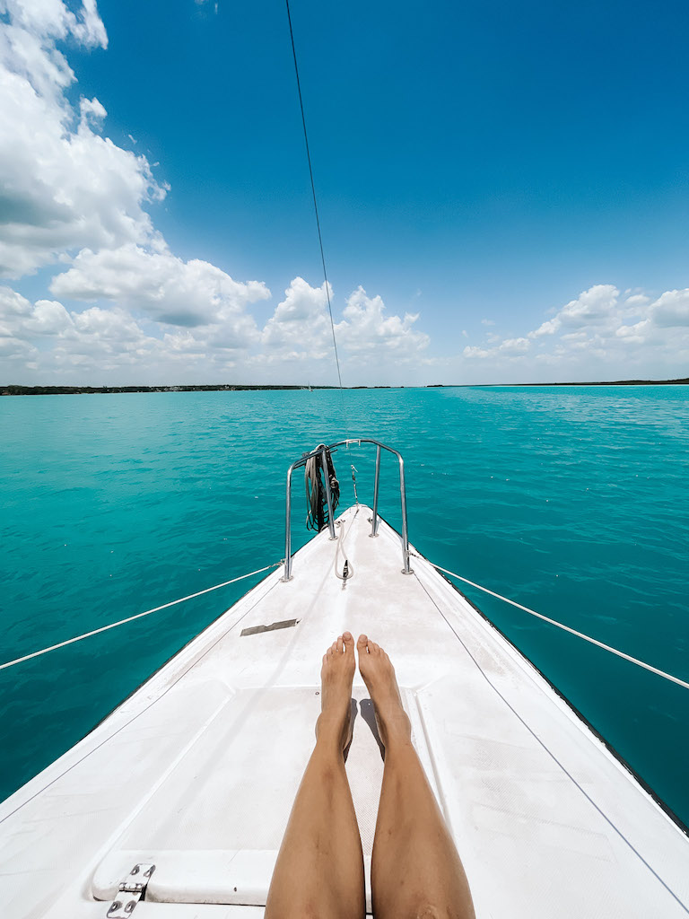 A woman's legs extended at the bow of a white catamaran in the blue sea.