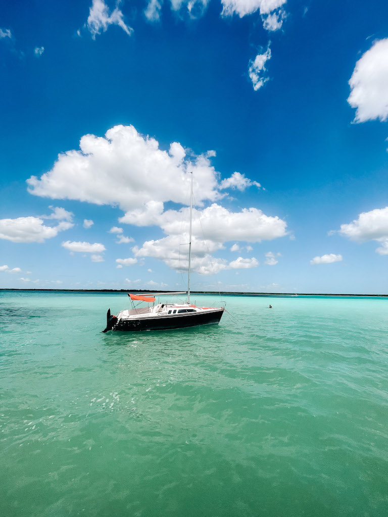 Black, white and red sailing catamaran in turquoise water, the ky is blue with some clouds.