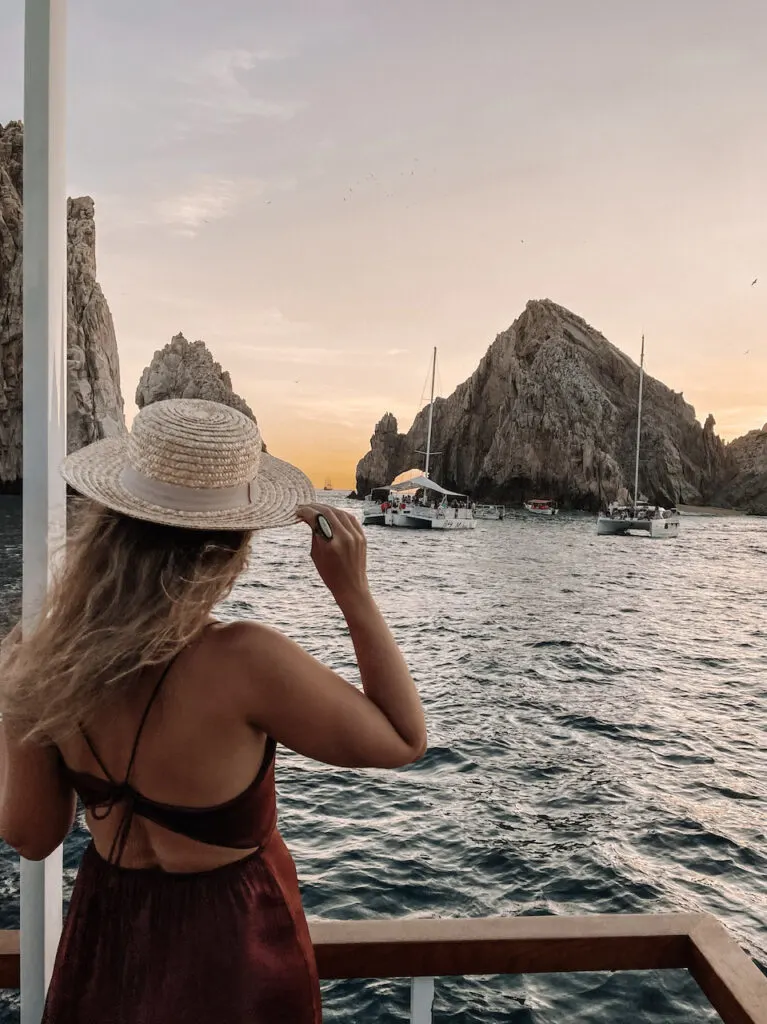 A woman watching rock formations from a boat's deck during sunset 