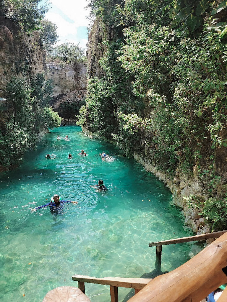 People swimming in a turquoise canal, whose walls are covered by plants.