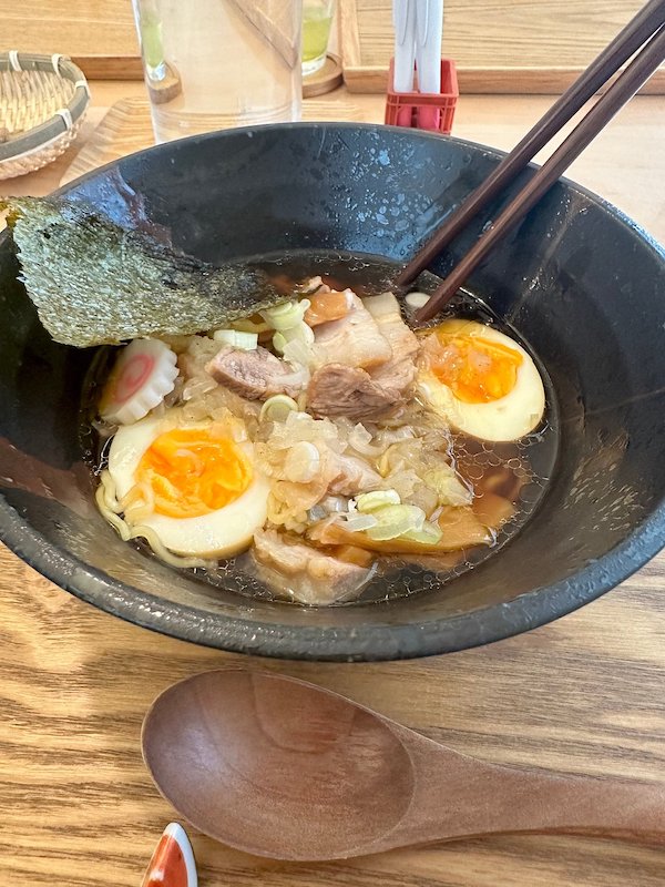 A black bowl of ramen with eggs and meat inside.